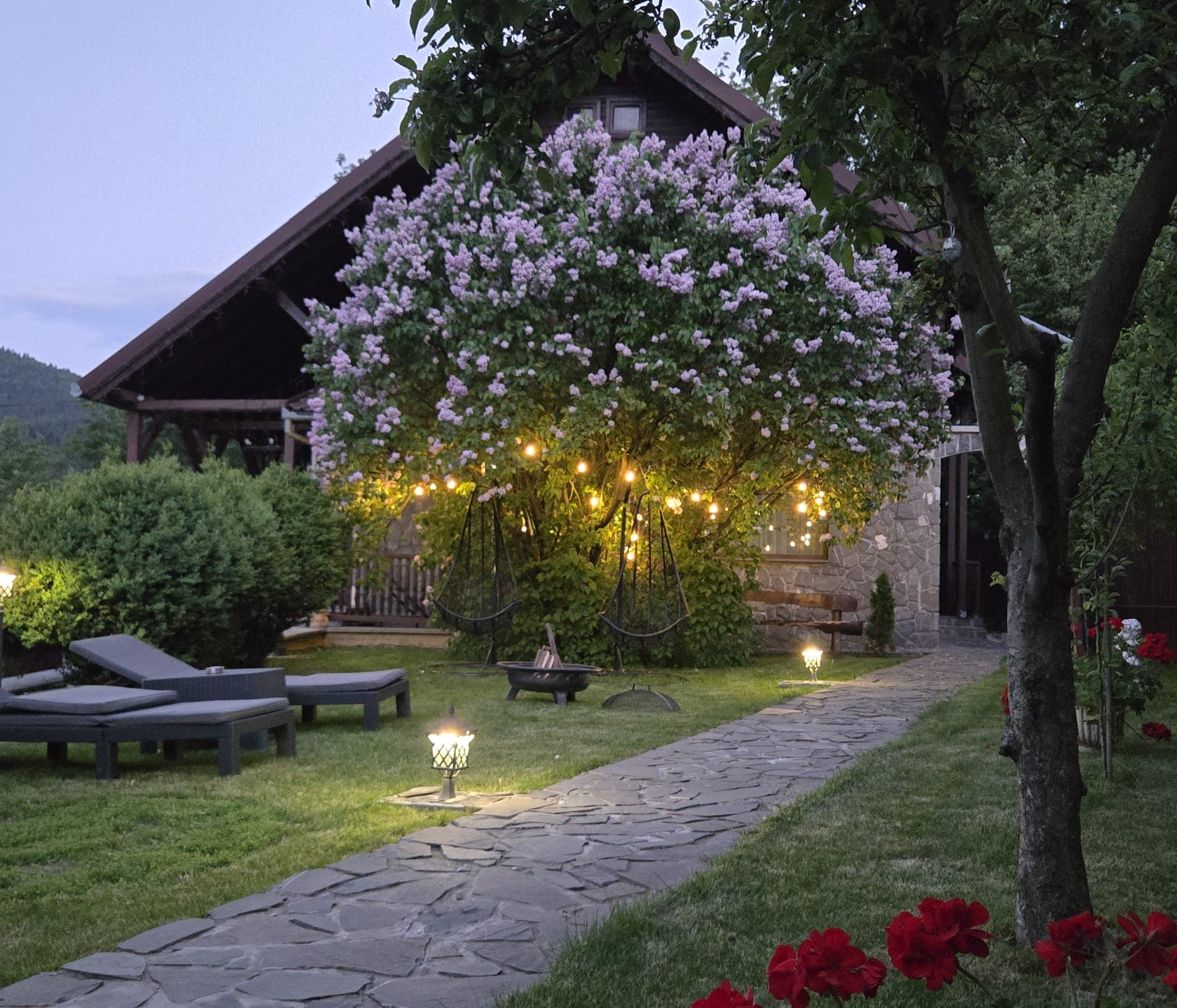 Grădina vilei seara, cu liliac înflorit și luminițe calde