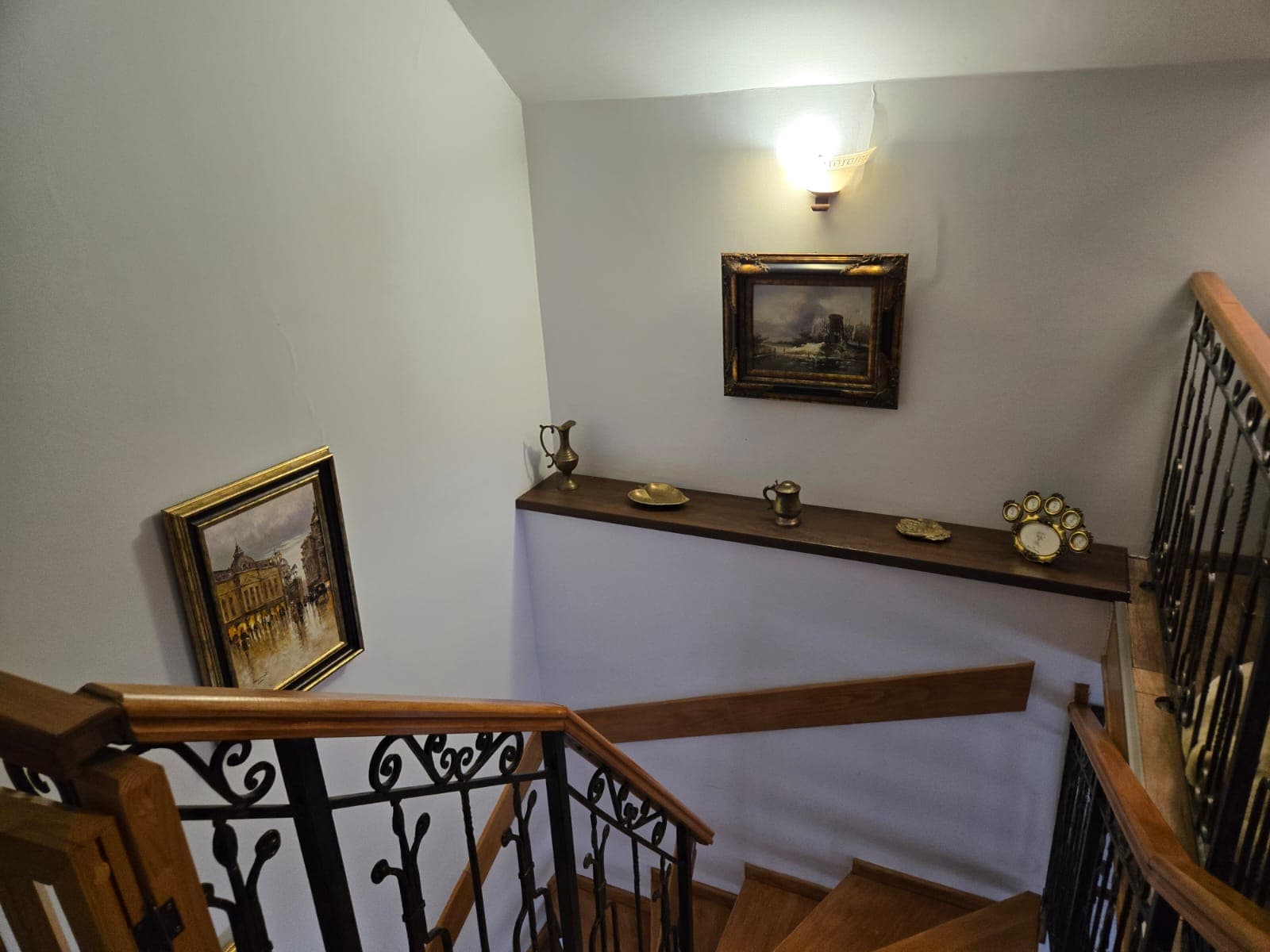 Scara interioară de lemn cu balustradă de fier forjat și tablouri pe pereți
